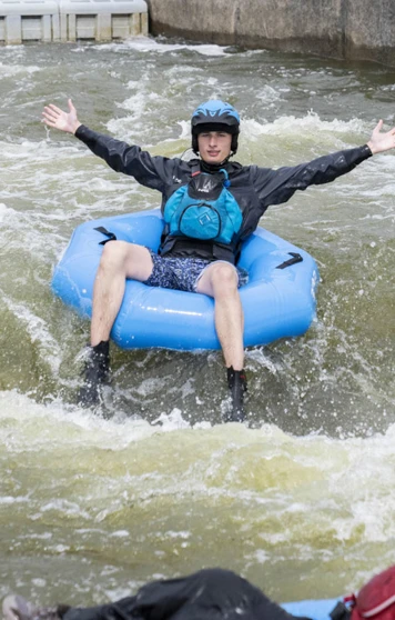 A student with arms outstretched riding a blue inflatable ring on a whitewater course. A student with arms outstretched riding a blue inflatable ring on a whitewater course.